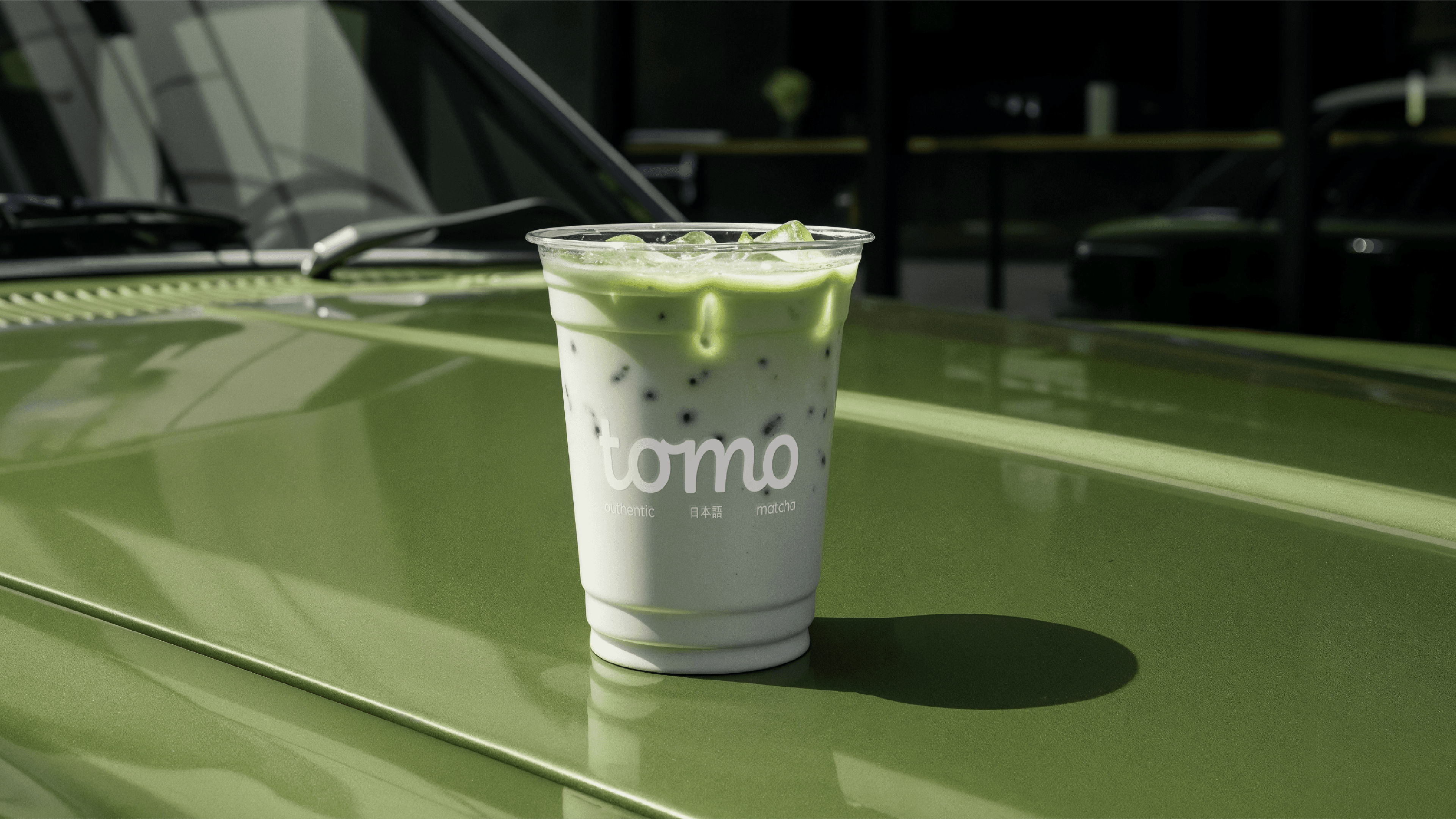 Tomo branded takeaway cup on a green car bonnet